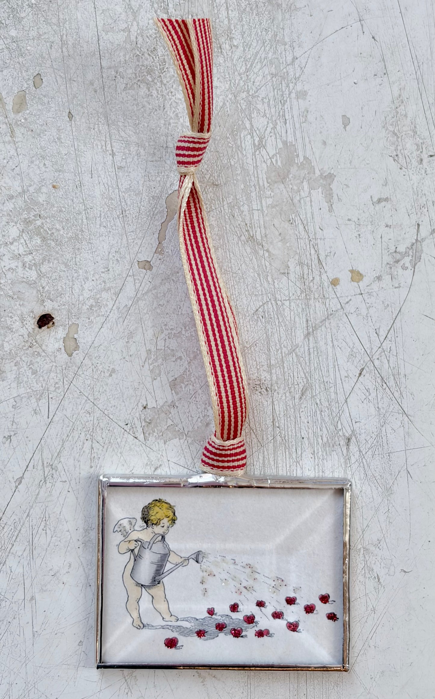 Decorative angel ornament with red and white striped ribbon on a textured surface