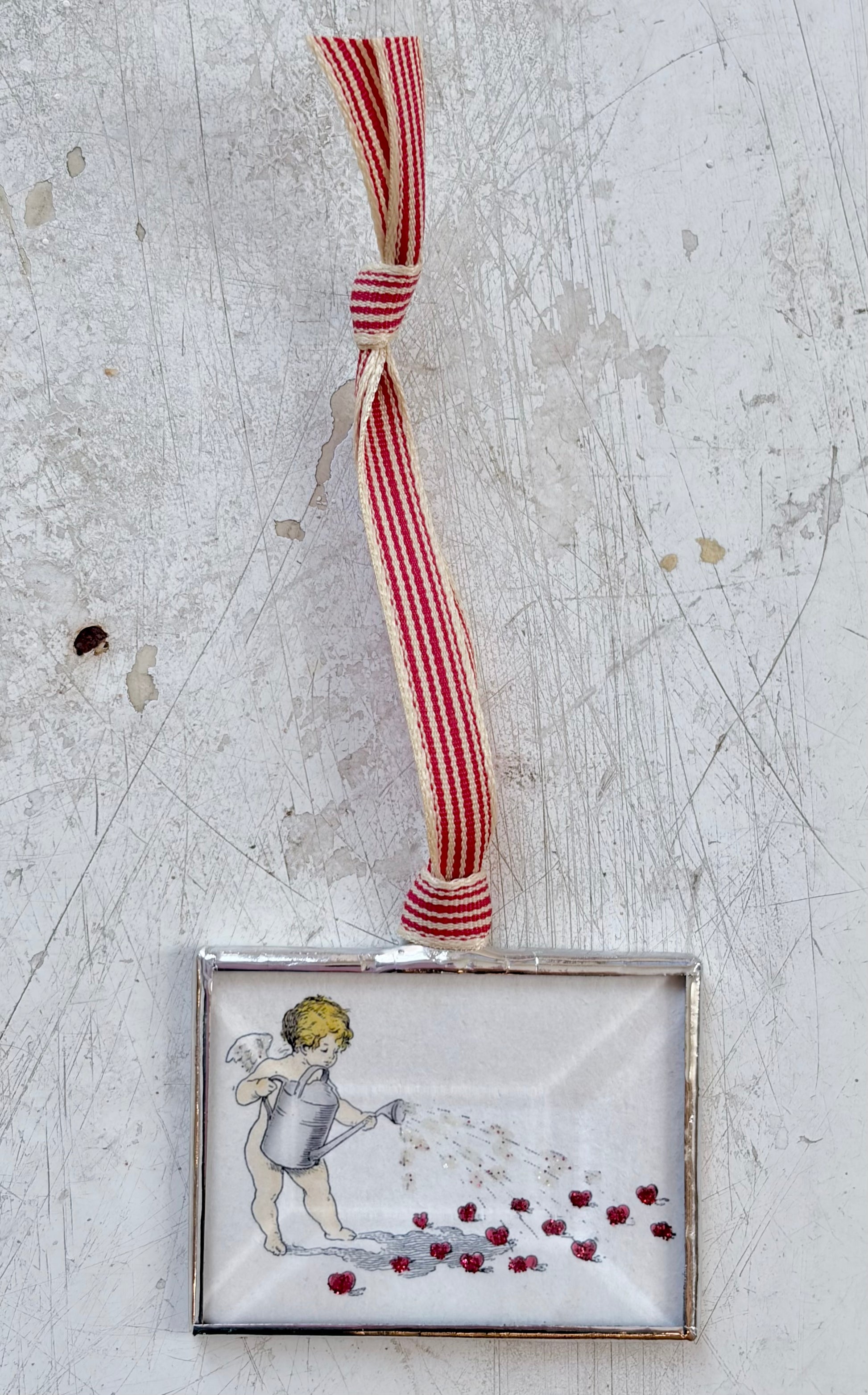 Decorative angel ornament with red and white striped ribbon on a textured surface